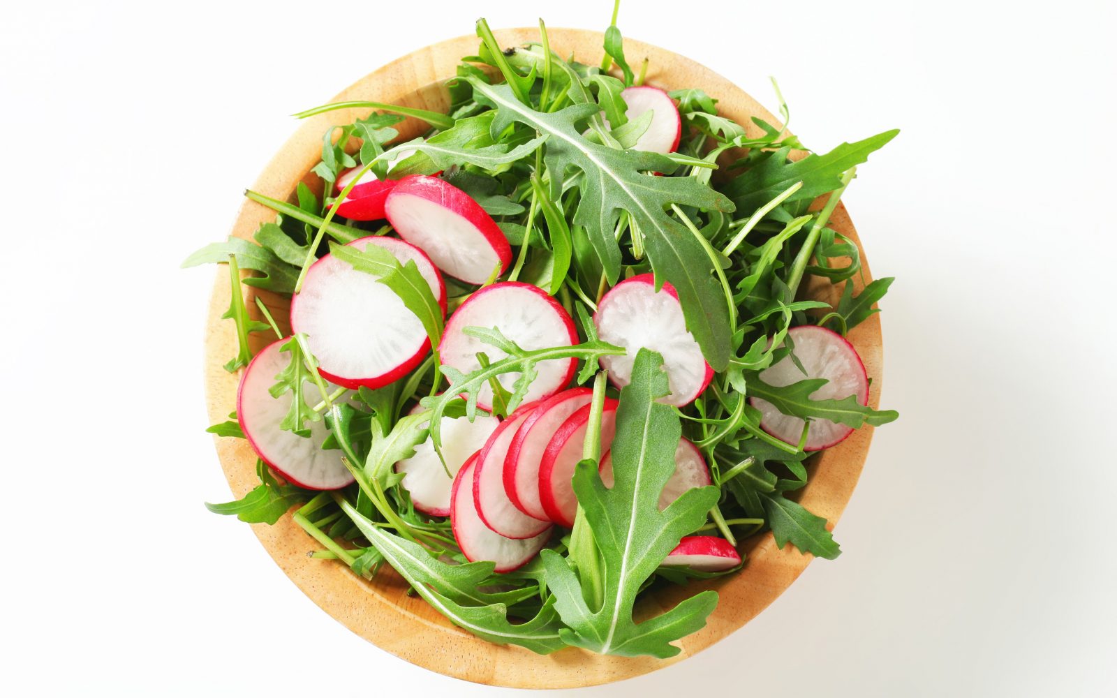 Na sliki je lesena skleda z zdravo pomladno solato iz rukole in narezanih redkvic, ki jo lahko postrežemo kot prilogo k velikonočni pojedini.