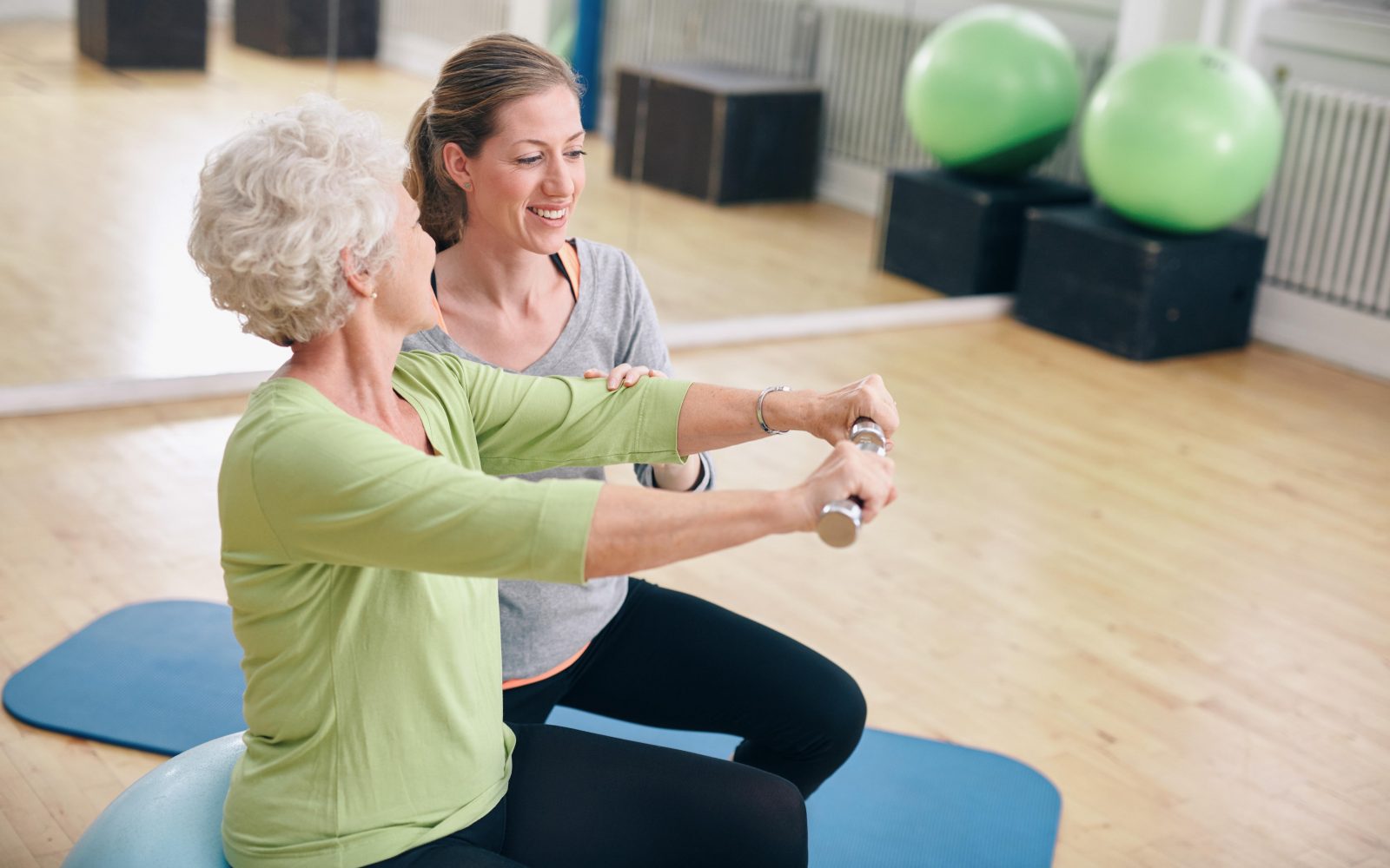 Trenerka pomaga starejši ženski izvajati vaje z utežmi za izboljšanje kognitivnih sposobnosti in zmanjševanje tveganja za demenco.