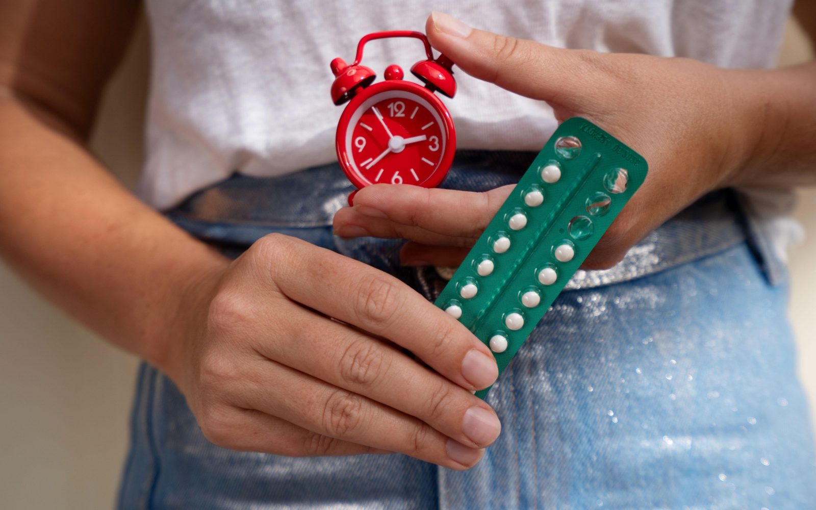 Ženska drži škatlico kontracepcijskih tabletk - hormonska kontracepcija kot eden od vzrokov za izostanek menstruacije ali lažje krvavitve.