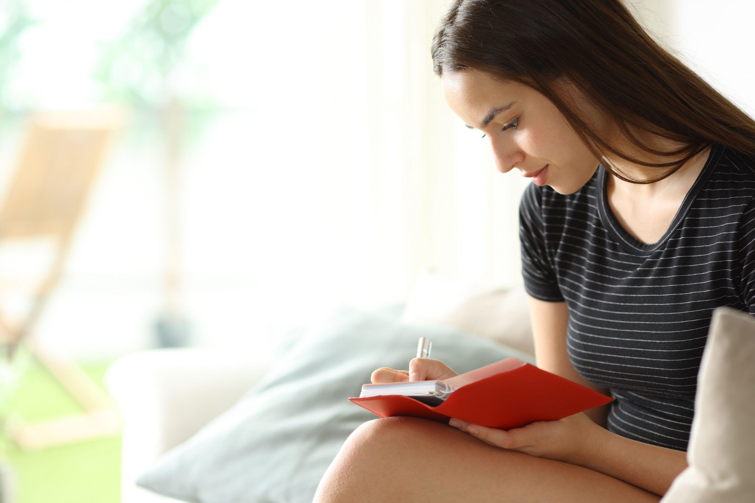 Mlada ženska piše dnevnik, kar je strategija, ki pomaga mladim strukturirano predelati skrbi in zmanjšati vsakodnevno anksioznost.