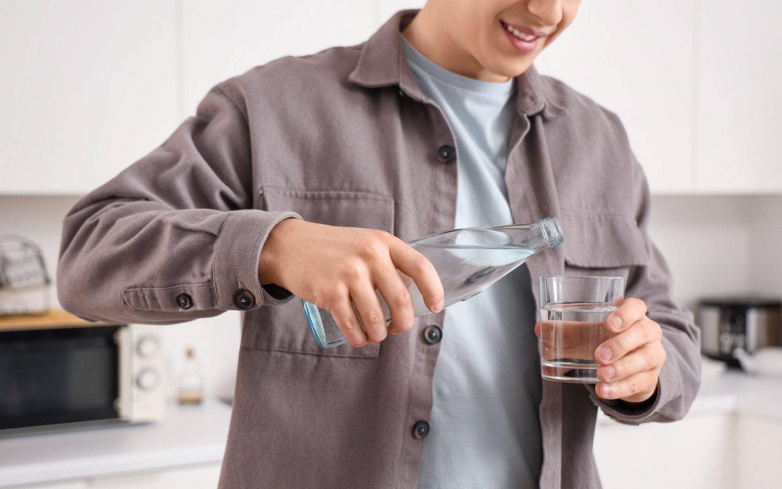 Mlad moški toči vodo v kozarec, saj zadostna hidracija pomaga ohranjati ravnovesje v črevesju, kar izboljšuje kakovost spanca.