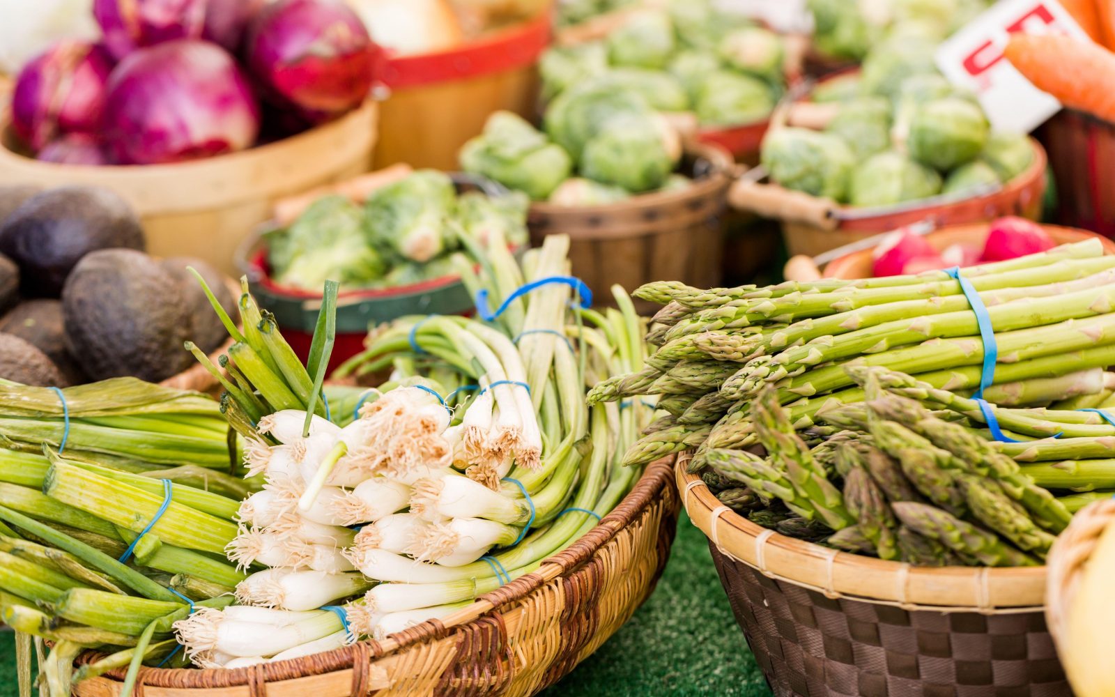 Košare na tržnici, polne sveže sezonske pomladne zelenjave, kot so šparglji, mlada čebula, redkvice, špinača, odlična za zdrave pomladne obroke.