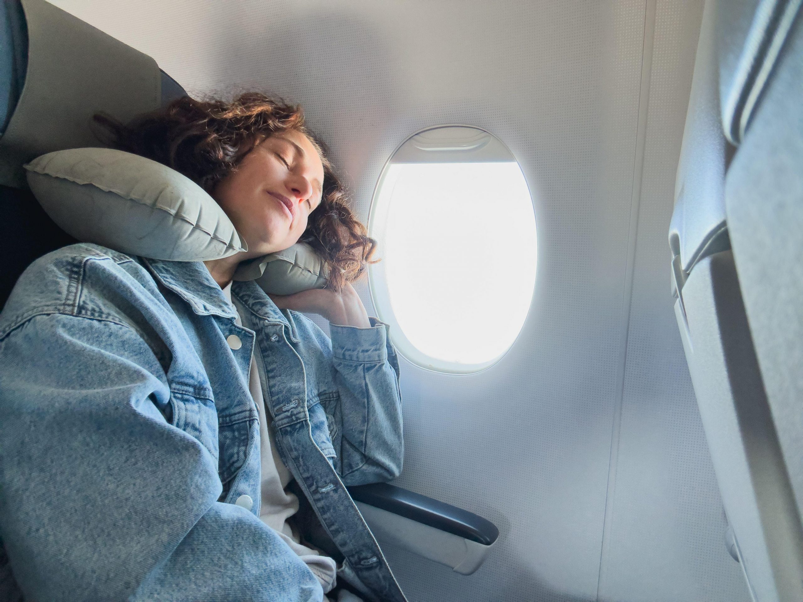Mlada ženska spi na letalu z blazino za vrat za bolj udoben počitek in let.