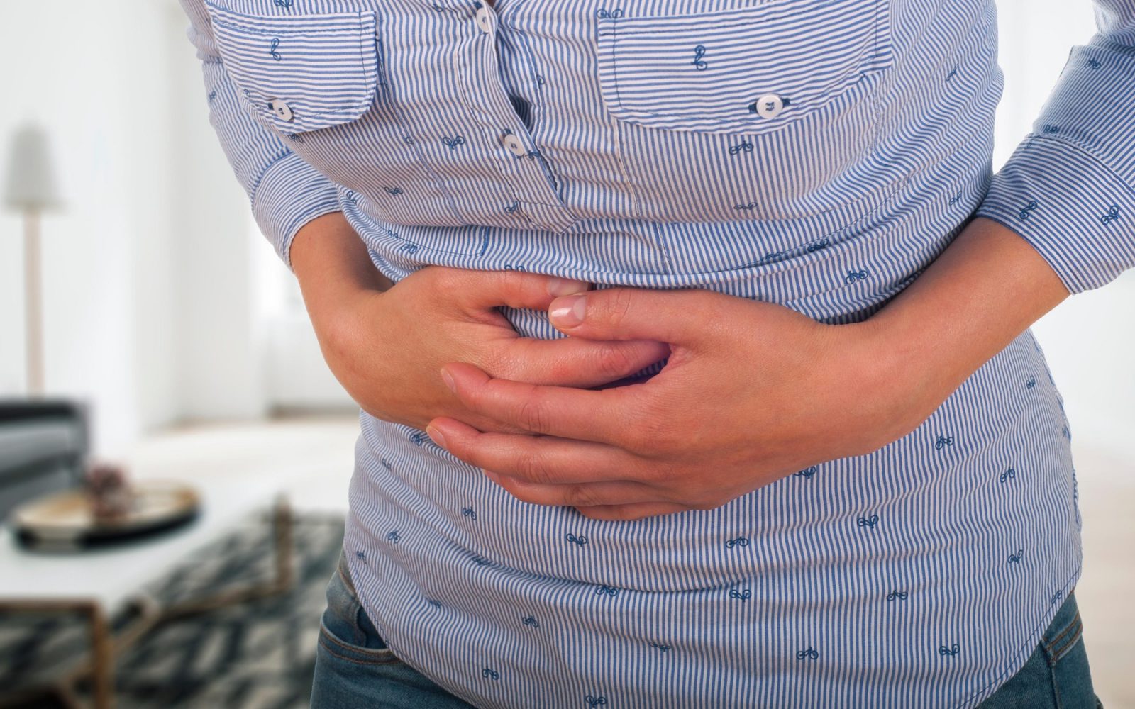 Ženska z rokami na spodnjem delu trebuha, ki kaže znake bolečin v trebuhu – mogoči simptom divertikuloze ali drugih prebavnih težav.