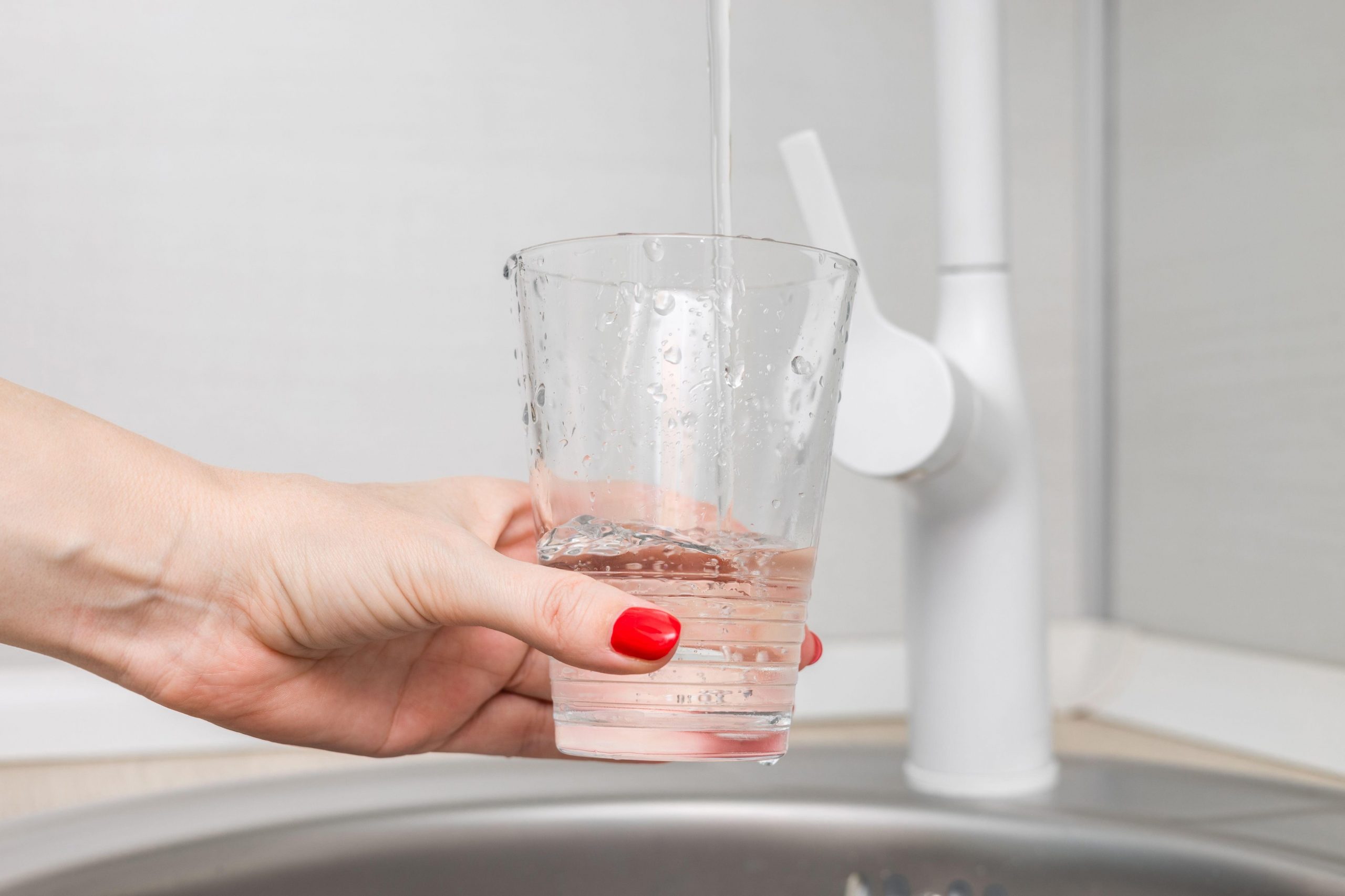 Ženska si naliva kozarec vode – pomemben korak k hidraciji za lajšanje bolečin v trebuhu in boljšo prebavo.