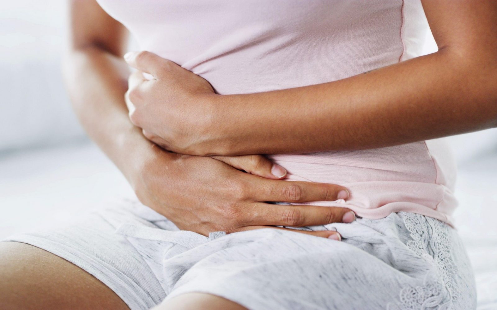 Ženska, roke in bolni v postelji z bolečinami v želodcu, menstruacijskimi krči in simptomi IBS. Ženska, nelagodje in tveganje za zdravje v domači spalnici