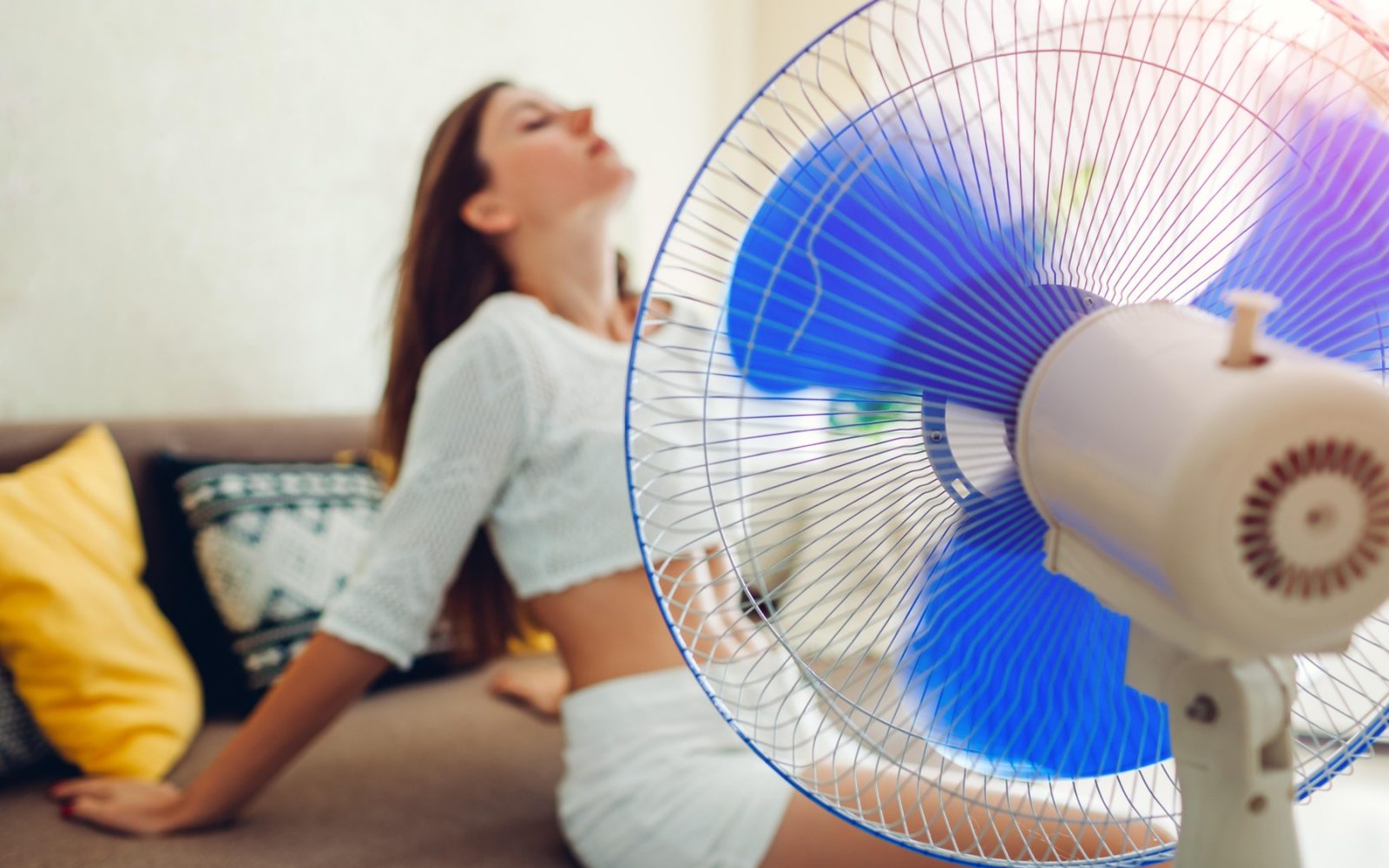 Mlada ženska se doma ohlaja na kavču ob ventilatorju zaradi poletne vročine.