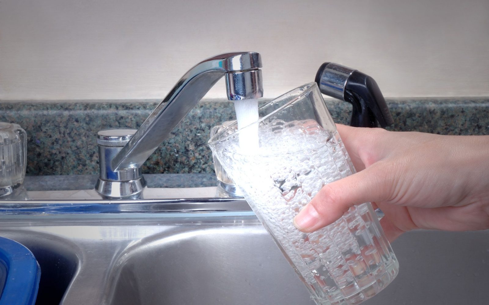 Roka drži kozarec, v katerega iz pipe teče voda – opozorilo o možni nevarnosti pri pitju določenih vrst vode iz pipe.