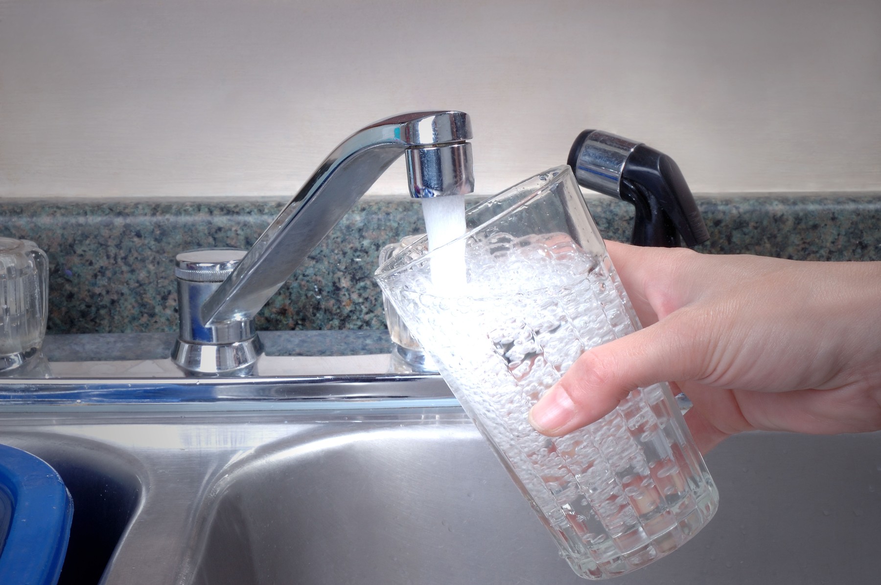 Roka drži kozarec, v katerega iz pipe teče voda – opozorilo o možni nevarnosti pri pitju določenih vrst vode iz pipe.
