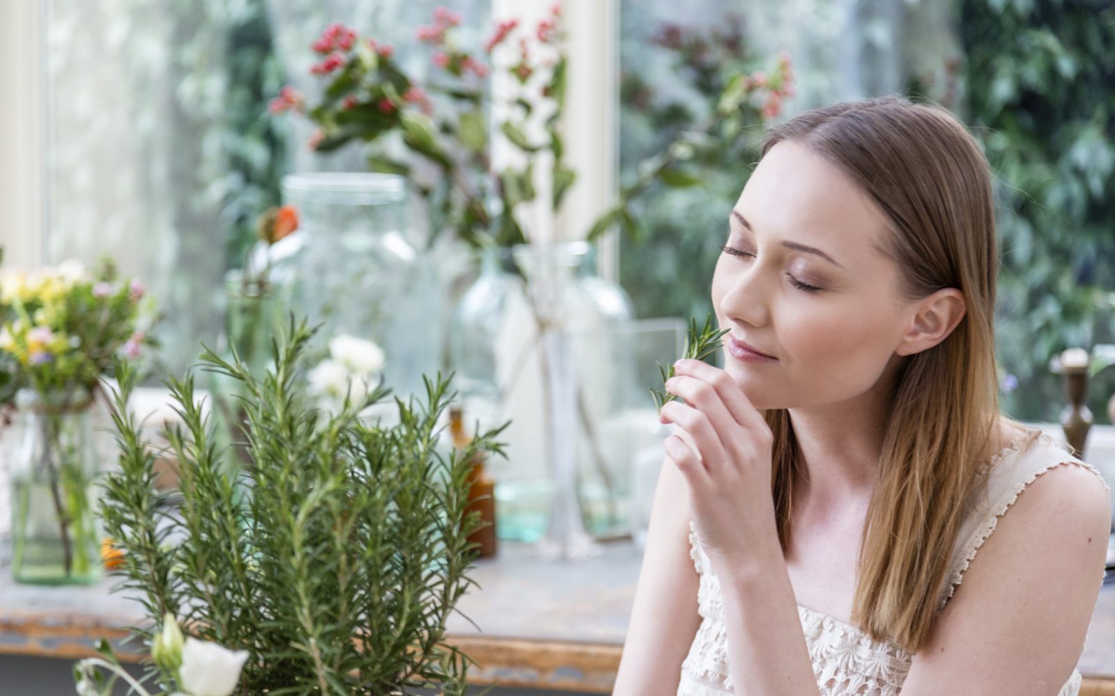 Ženska z zaprtimi očmi vonja rožmarin - rastlino, ki ima številne koristi za zdravje možganov, spomin, notranji mir in splošno zdravje.