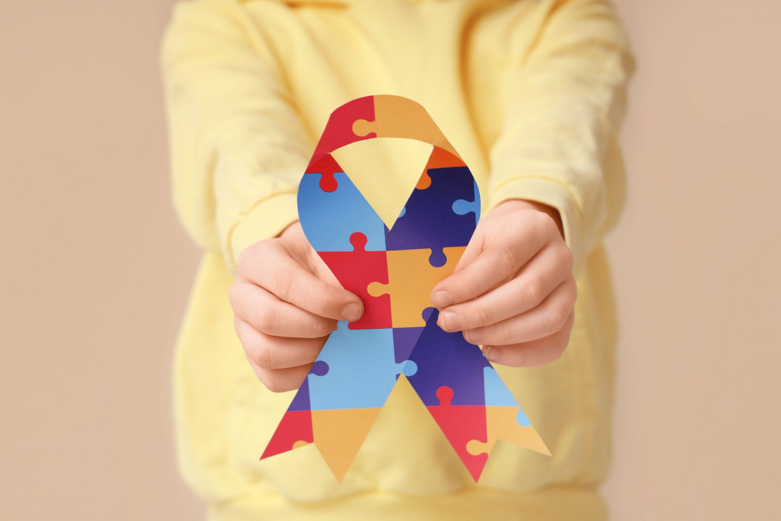 Deček z avtistično motnjo v rumenem puloverju drži pisano pentljo, ki je simbol motenj avtističnega spektra.