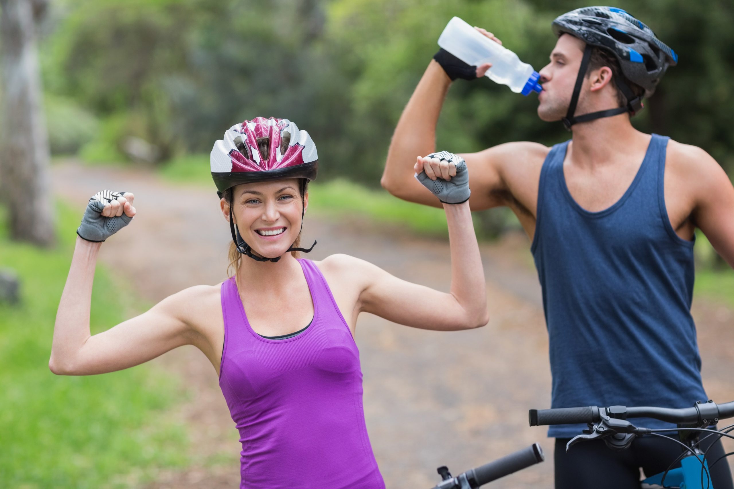 Ženska in moški na kolesu, ki sta varna v prometu - nosita živa oblačila, zaščitno čelado, se hidrirata in upoštevata prometne predpise.