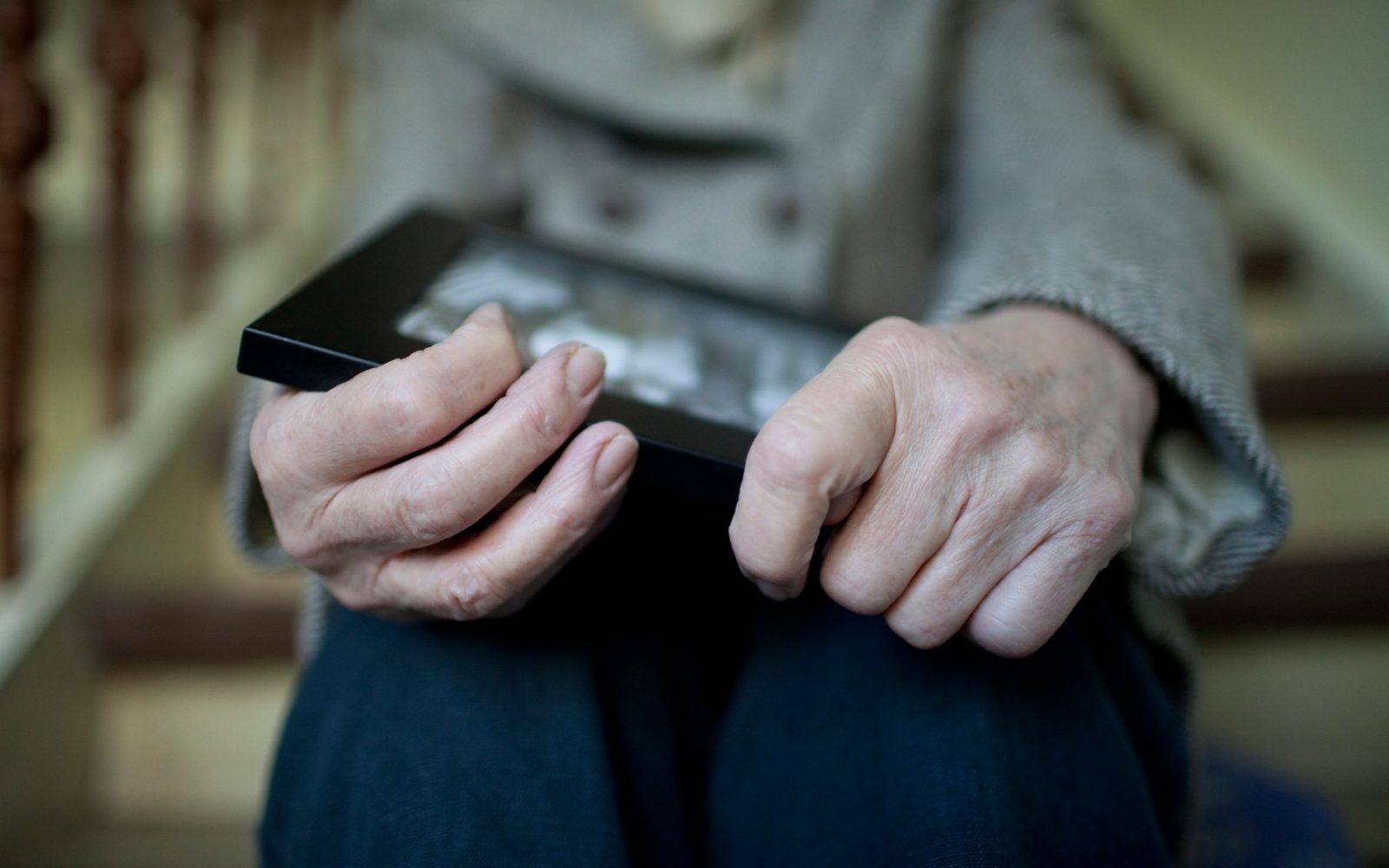 Starejša oseba, ki drži okvir s fotografijo, sedi zamišljena – simbol zgodnje demence in izgube spomina