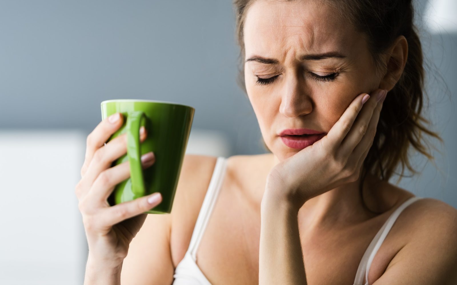 Ženska s skodelico, ki zaradi bolečine v zobeh trpi za bruksizmom