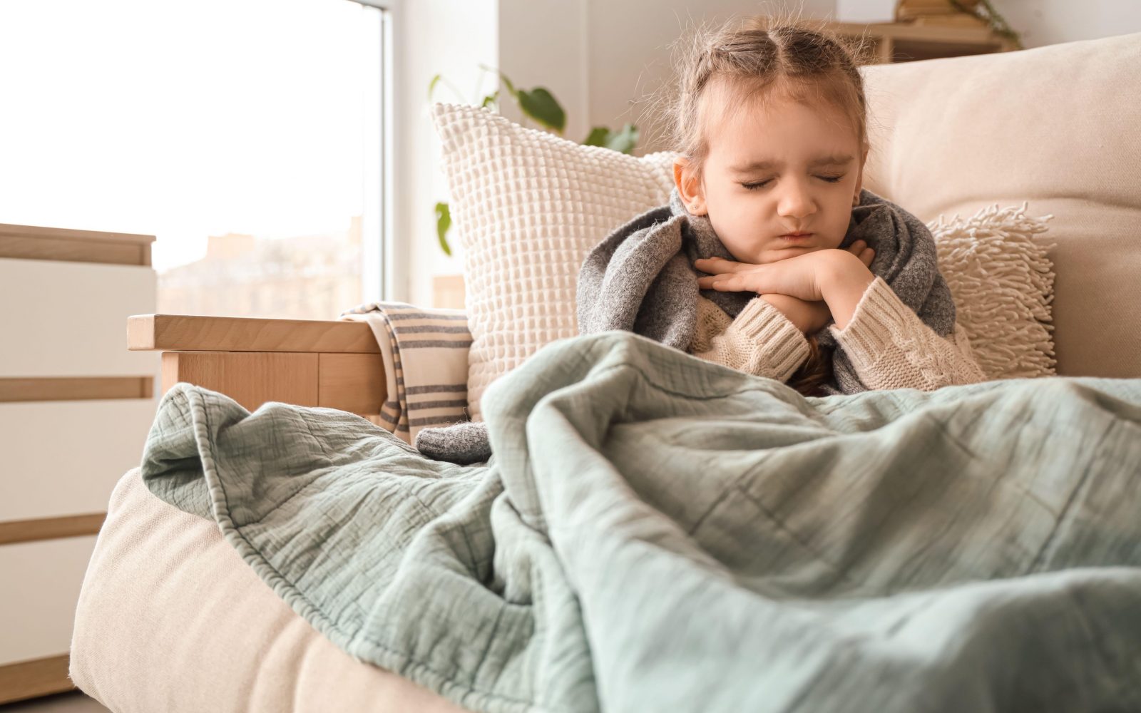 Majhna deklica se drži za vrat, ker jo močno boli grlo.