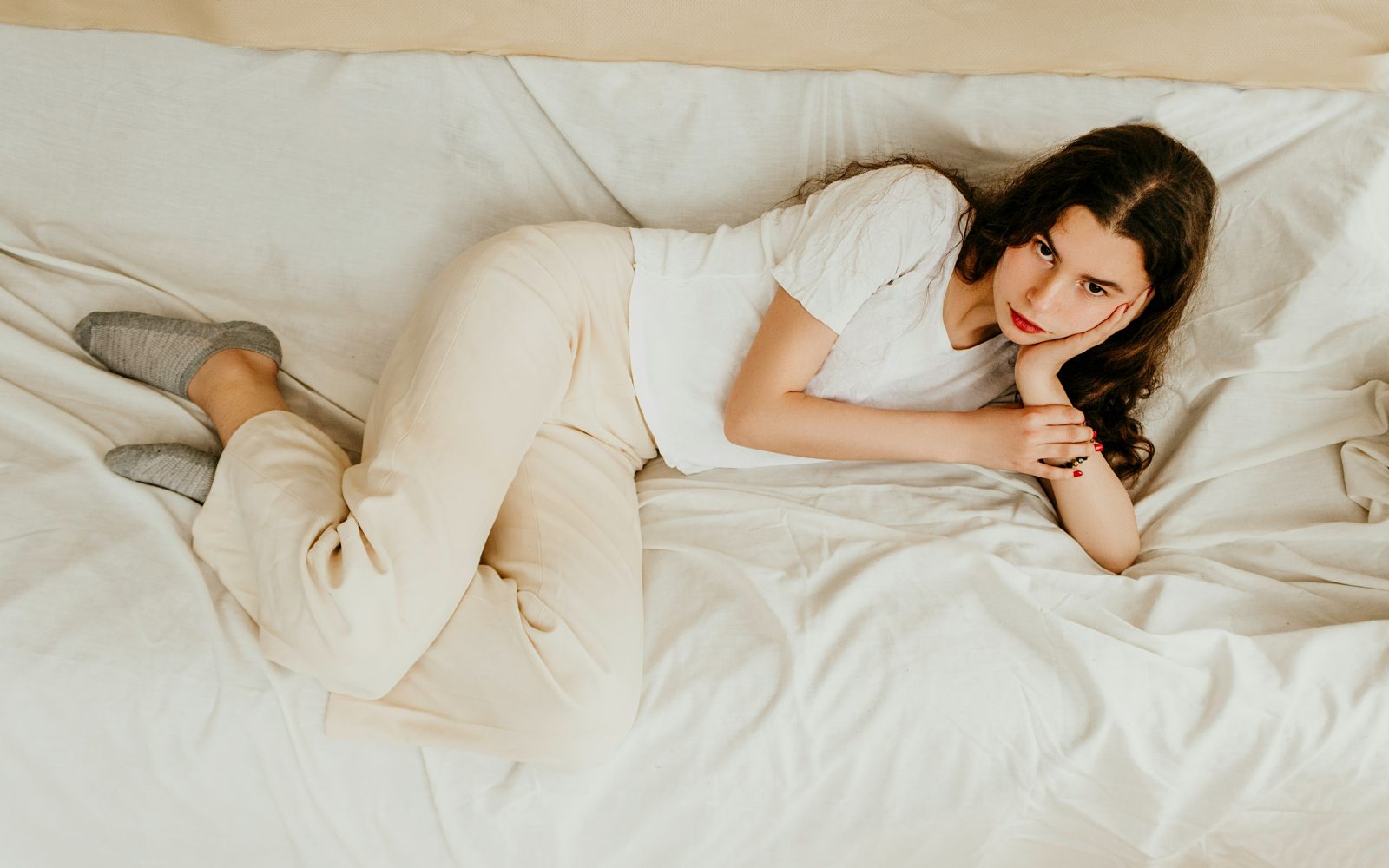 Nesrečna zamišljena ženska, oblečena v belo, z rdečimi nohti,. leži v postelji