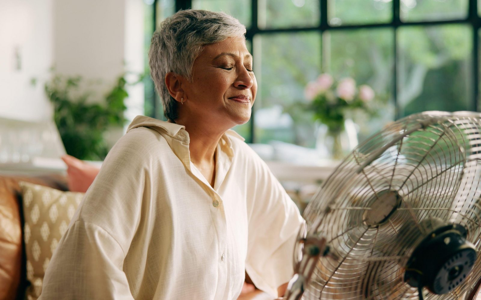 Starejša ženska v menopavzi, ki se hladi pred ventilatorjem, vročinski oblivi, simptomi menopavze
