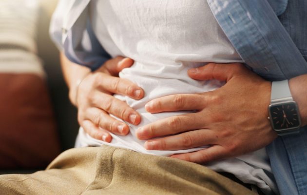Oseba z rokami na trebuhu, ki občuti bolečine ali napetost – znak prebavnih težav ali zaprtja.