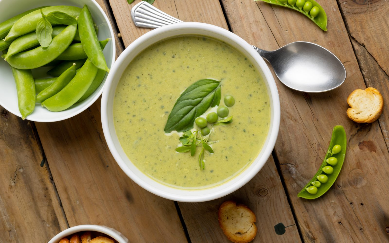 Skleda grahove juhe s krutoni na leseni mizi z žlico in grahom v posodici - lahek poletni obrok iz sezonskih sestavin.