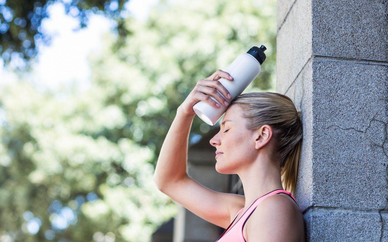 Ženska športnica v vročem dnevu drži flašo na glavi, hidracija, rehidracija, pitje tekočine