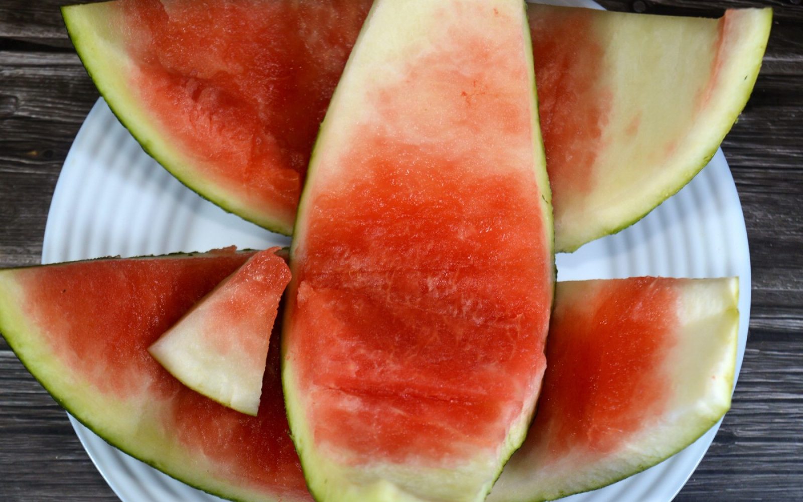Ostanki lubenice na belem krožniku, ki prikazujejo delno pojedeno rdečo sredico ter belo in zeleno lupino – poudarek na užitnem, a pogosto zavrženem delu lubenice.