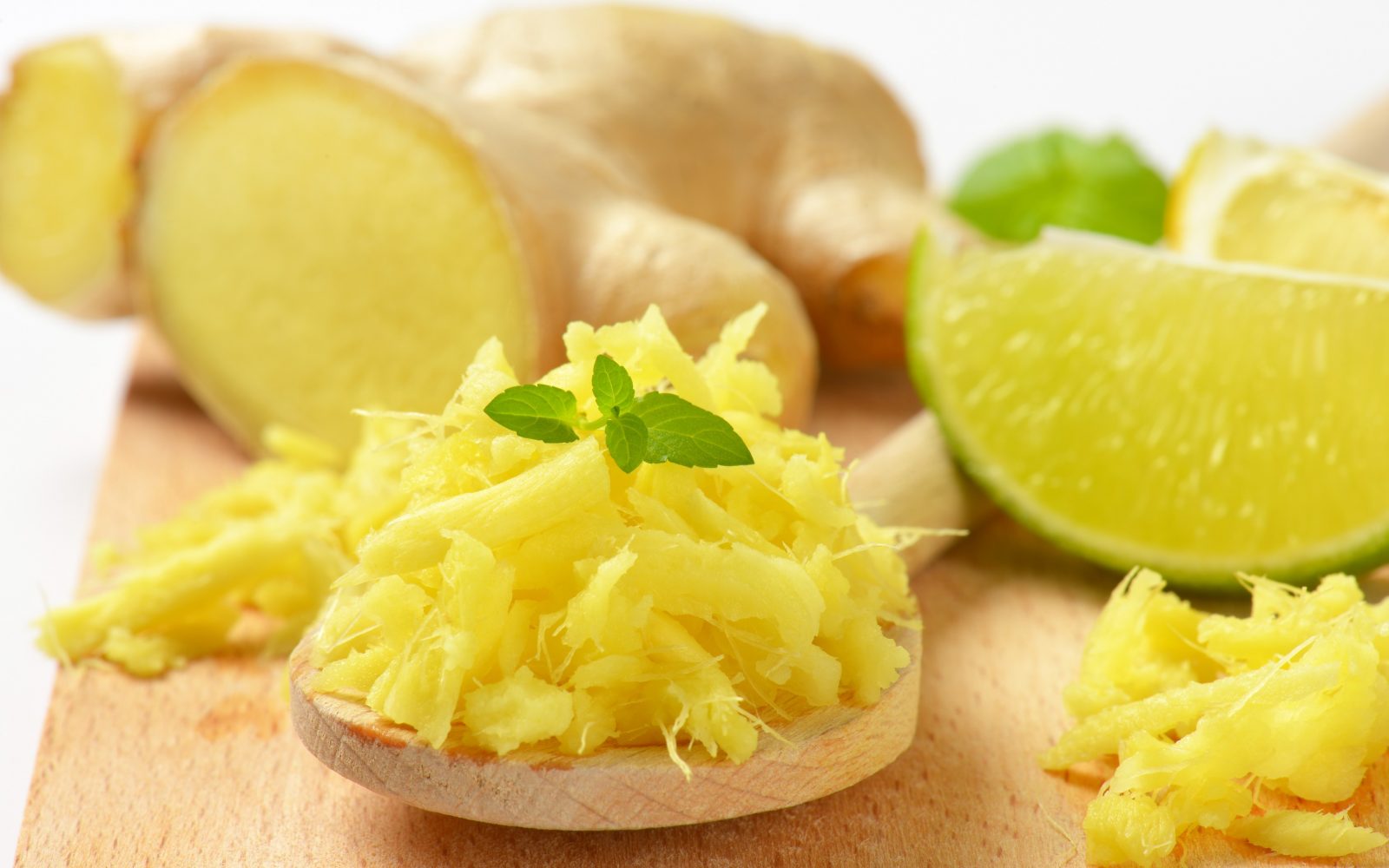 Svež nariban ingver na leseni žlici, ki je skupaj z medom naravno zdravilo proti sivenju las.