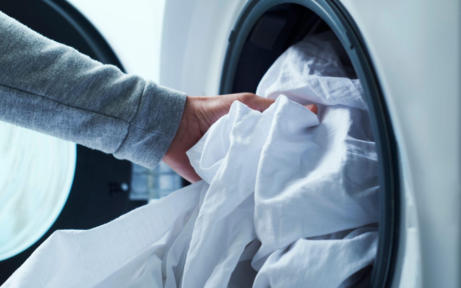 Moški daje posteljnino v pralni stroj – redno pranje za higieno in zdrav spanec