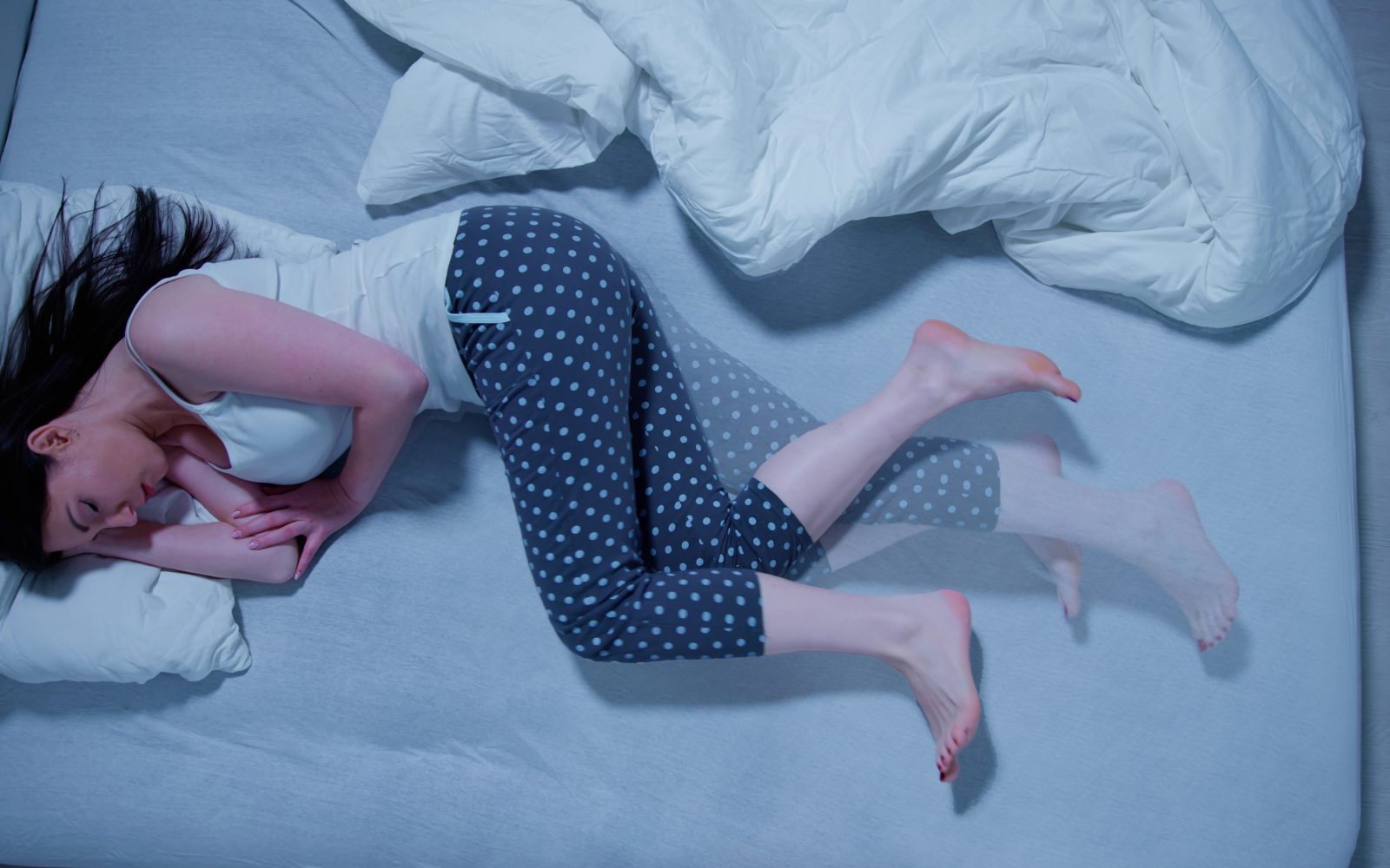 Ženska s sindromom nemirnih nog leži v postelji in spi