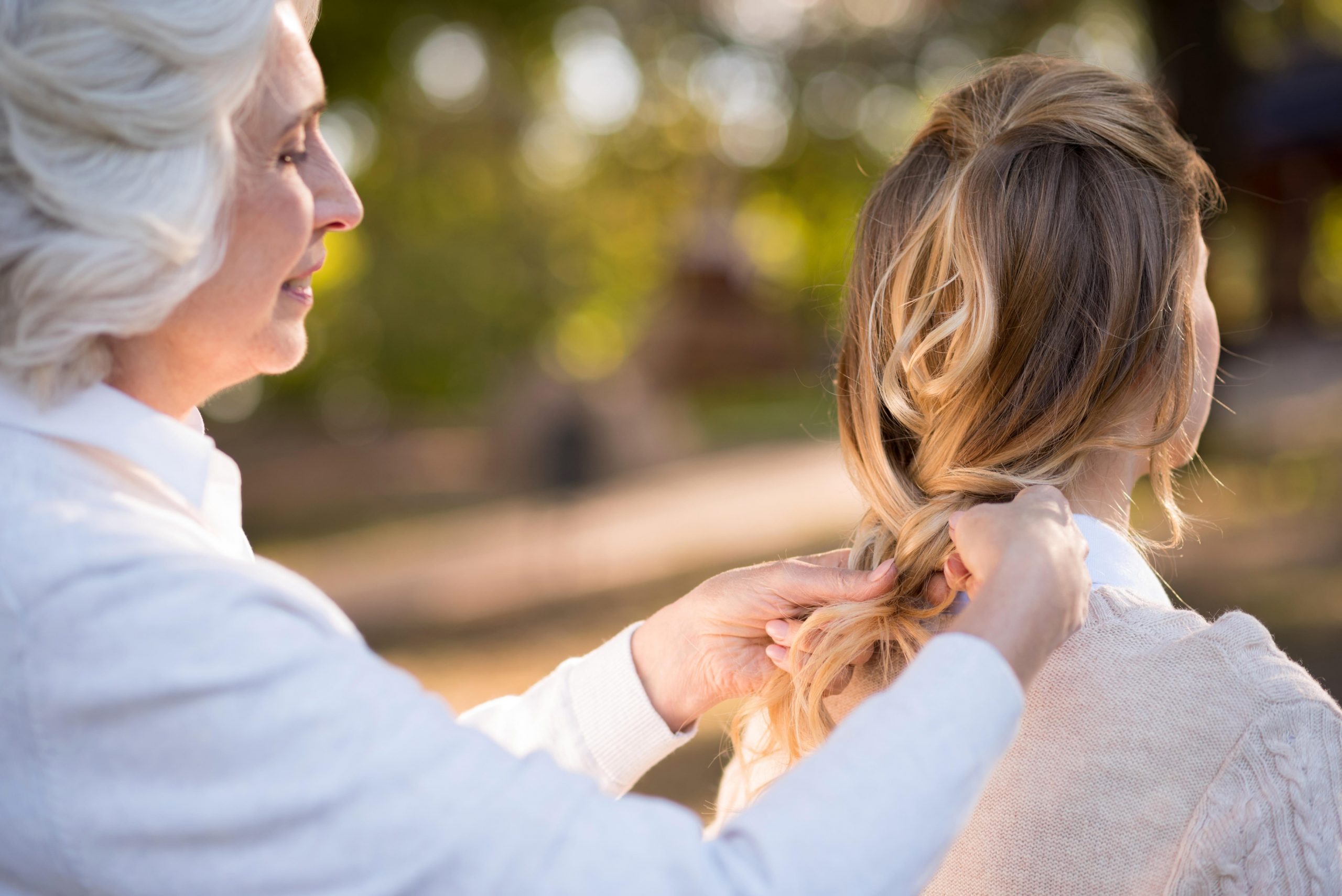 Starejša osivela ženska svoji hčerki spleta lase v kito - sivenje las je genetsko pogojeno