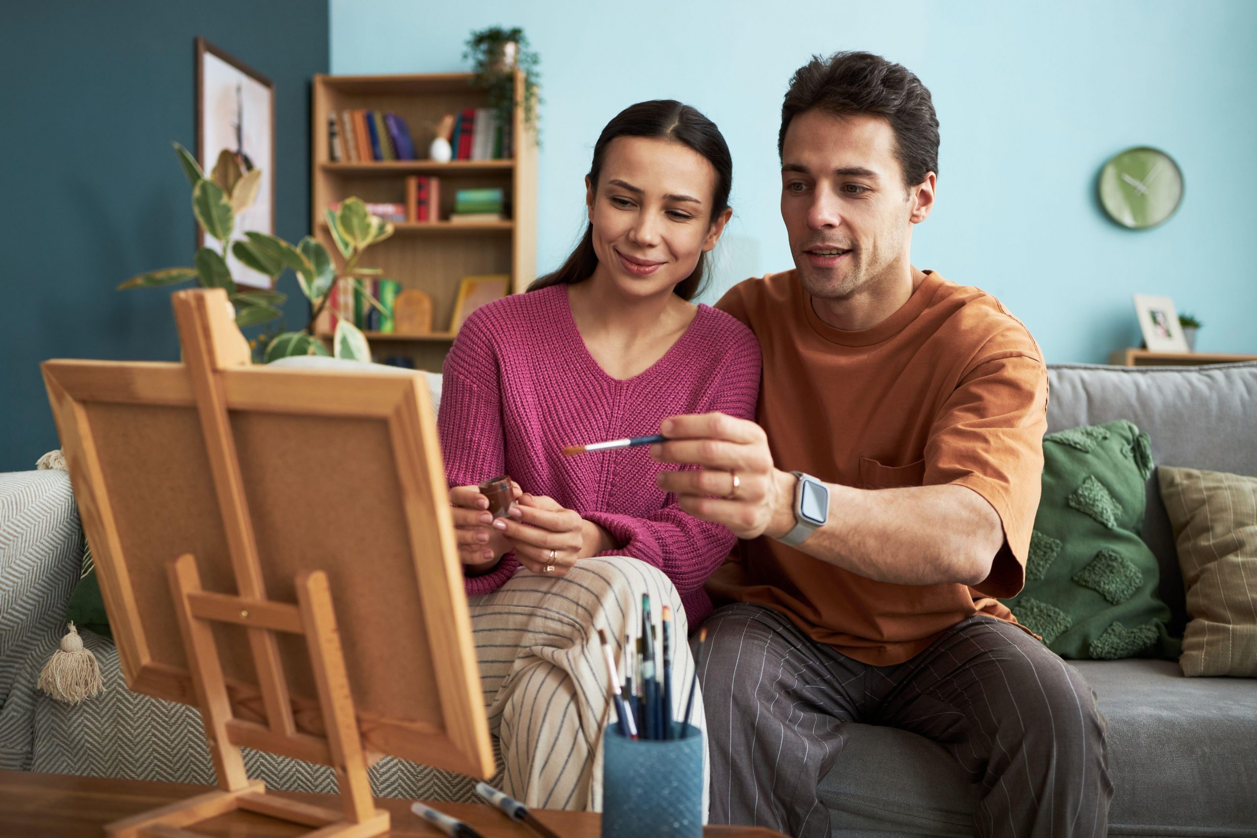 Mlad par sedi na kavču v dnevni sobi in slika sliko na platnu - način za povezovanje in obuditev iskrice v odnosu.