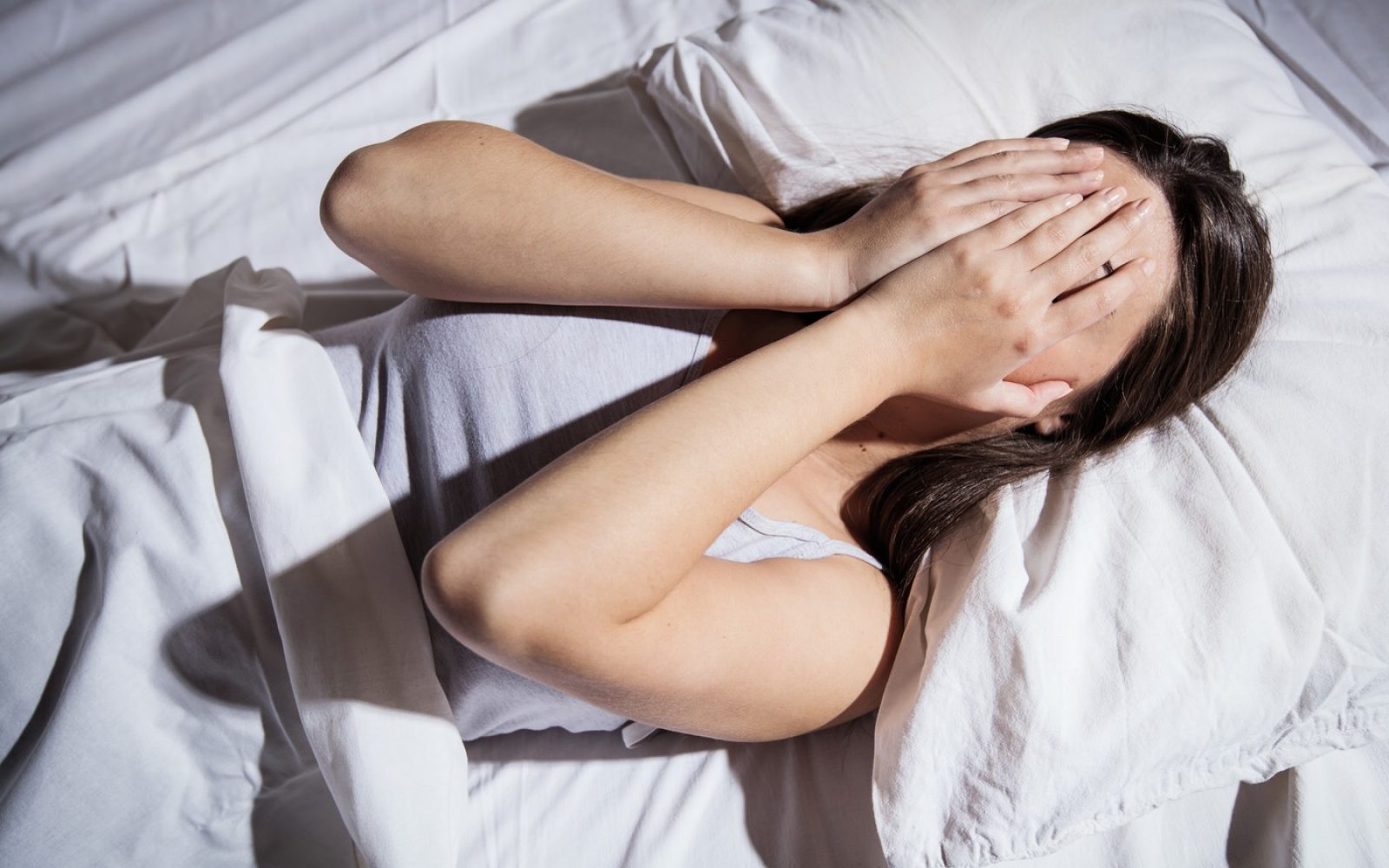 Ženska z nespečnostjo leži v postelji in si pokriva obraz z rokami.