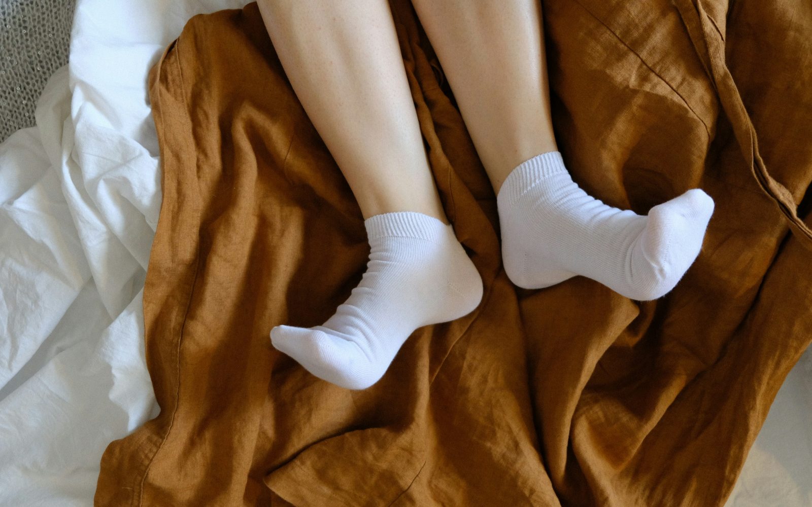 Noge z belimi nogavicami na postelji