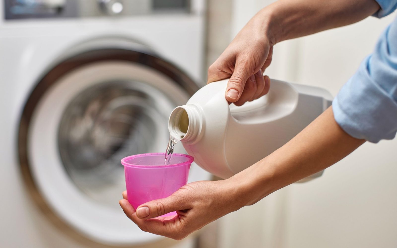 Oseba naliva pralni prašek v merilni pokrovček pred pranjem perila