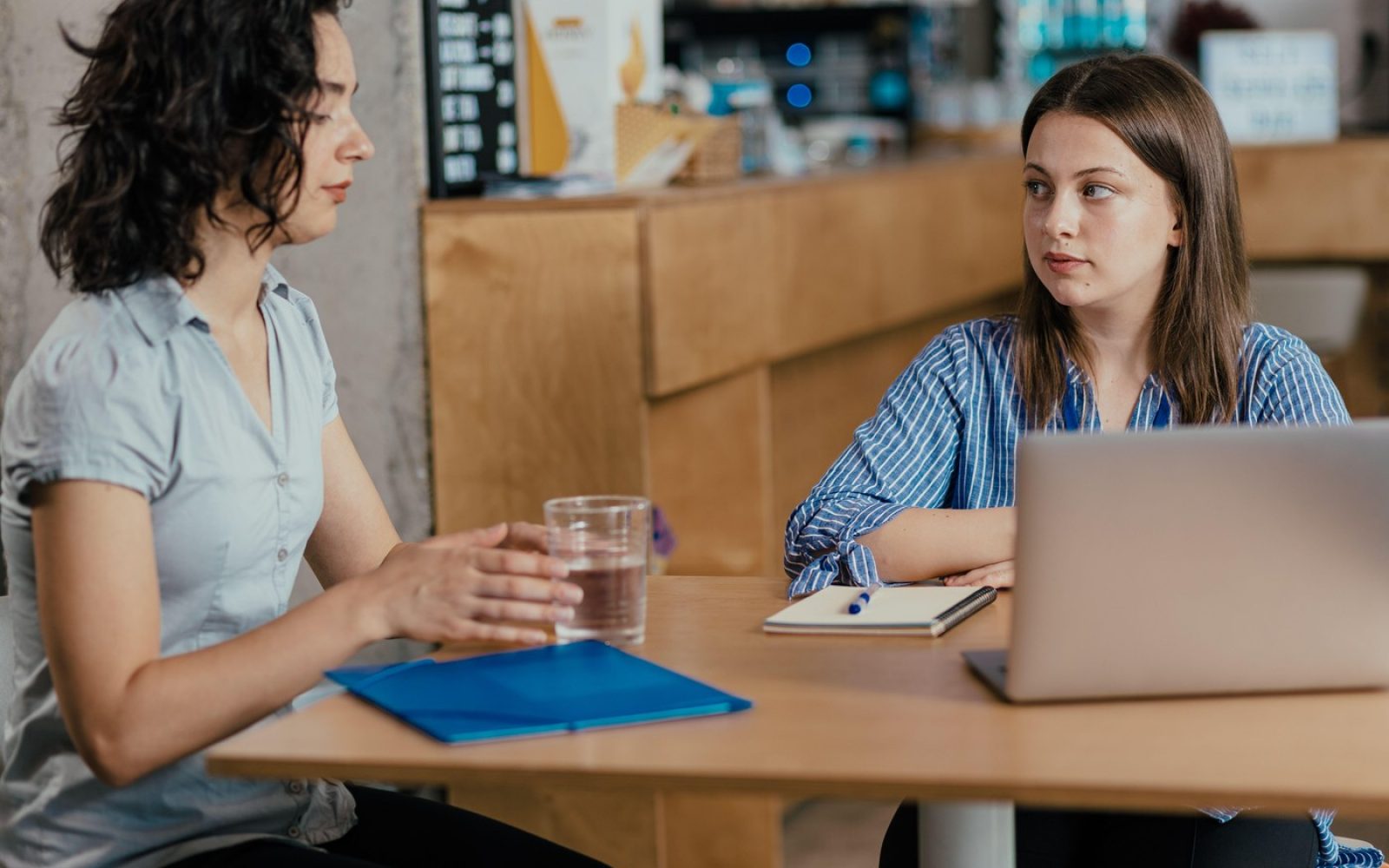 Dve sodelavki v pogovoru v pisarni, ena kaže resnost, druga posluša – prikaz čustvene nalezljivosti na delovnem mestu.