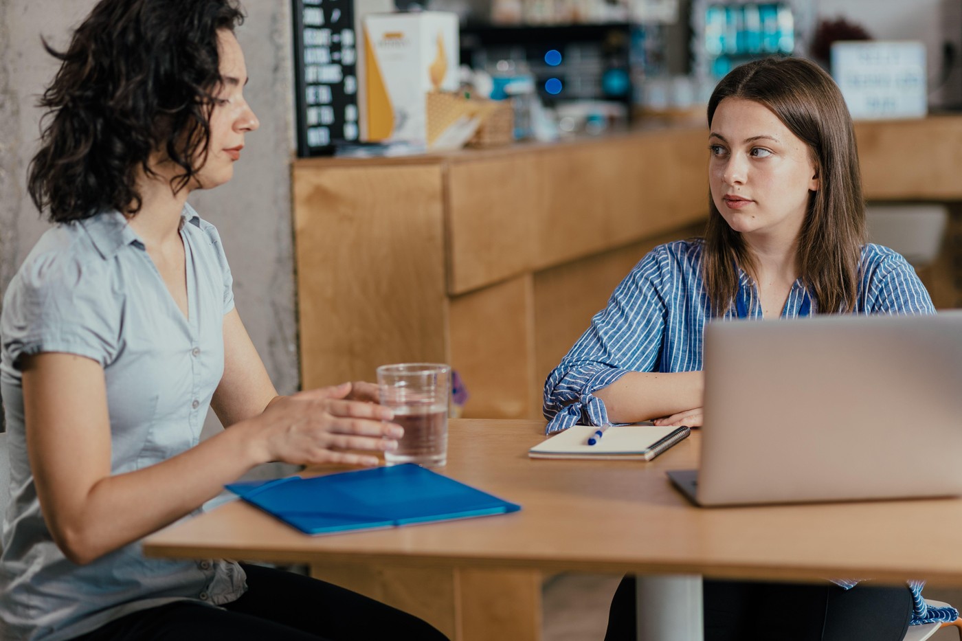 Dve sodelavki v pogovoru v pisarni, ena kaže resnost, druga posluša – prikaz čustvene nalezljivosti na delovnem mestu.
