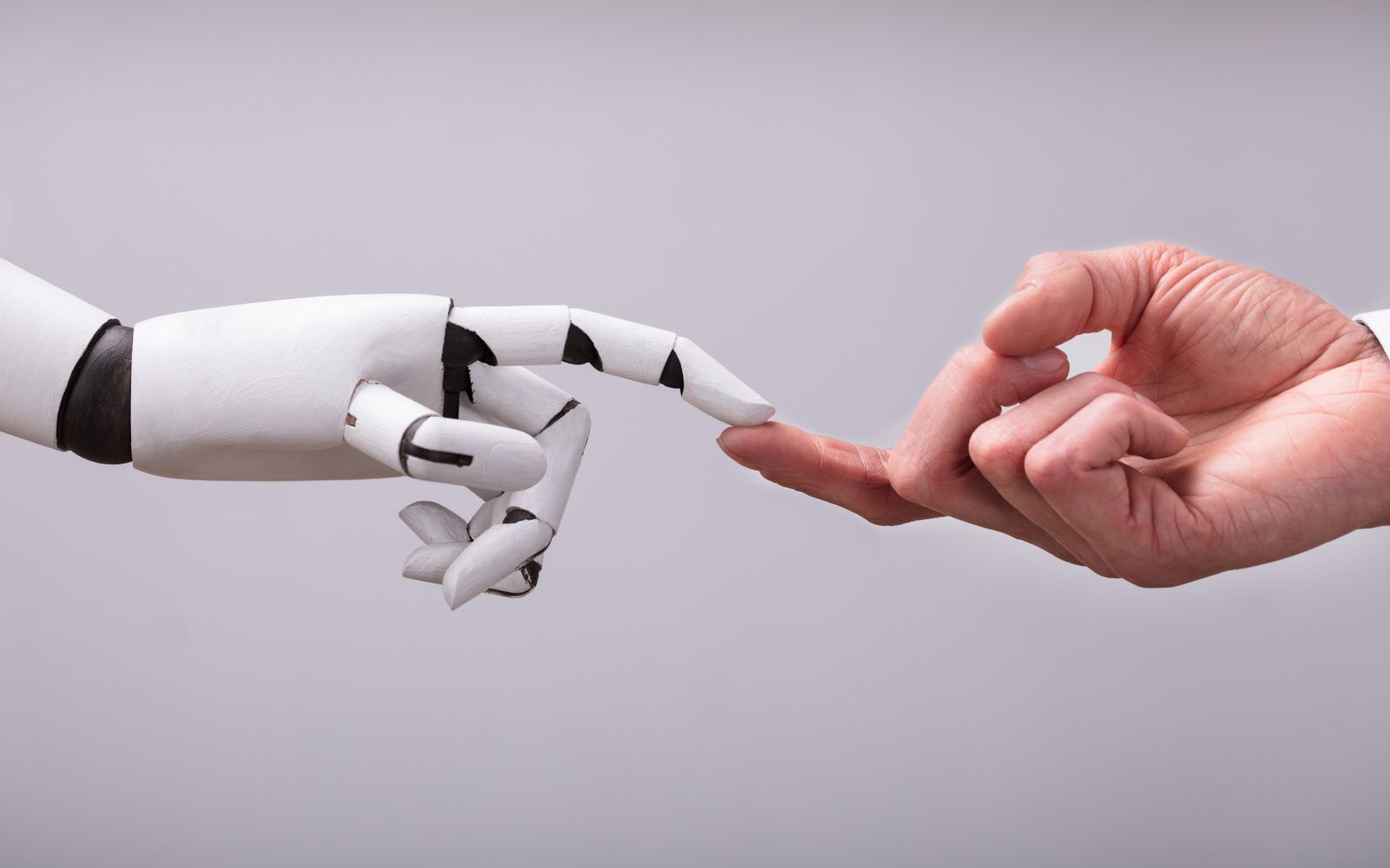 Roka humanoidnega robota in človeška roka se dotikata s prstom – simbol prihodnosti umetne reprodukcije in interakcije med človekom in robotom