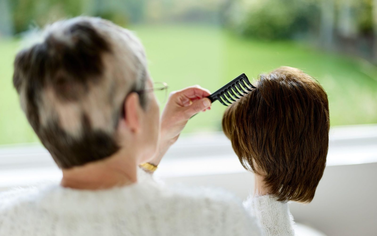 Starejša ženska češe lase mlajši ženski – simbolični prikaz dednega izpadanja las in skrbi med generacijami.