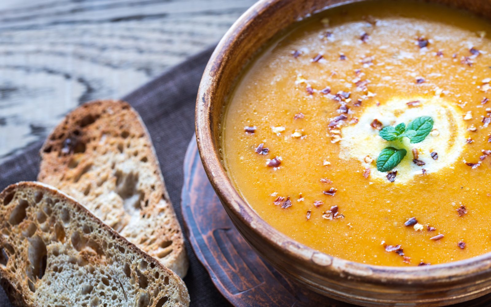 Zdrava jesenska bučno-ingverjeva juha v jušnem krožniku z dvema rezinama polnozrnatega kruha - popoln jesenski hranilen obrok.