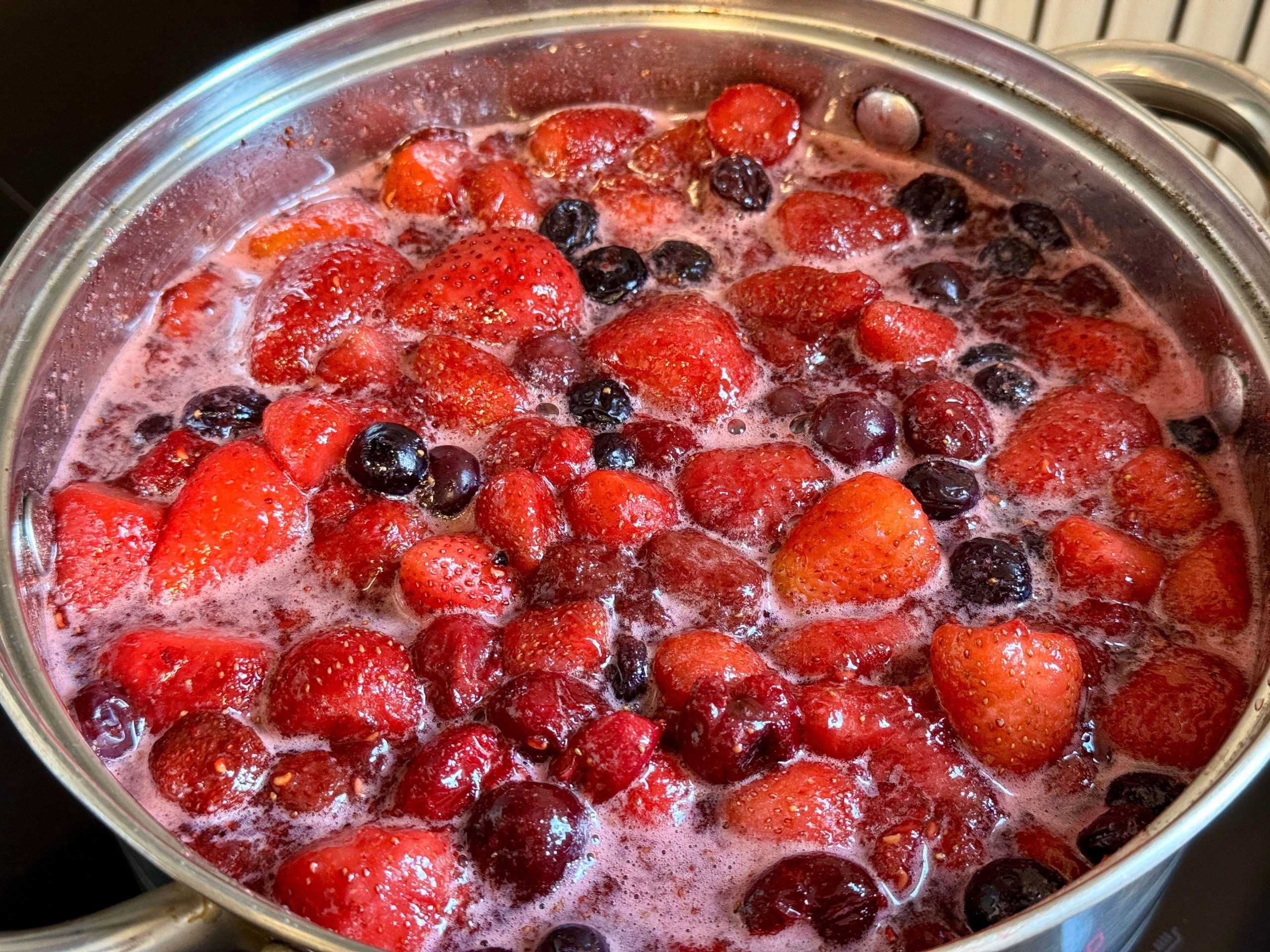 Jagode, borovnice, češnje in maline v loncu z vodo in sladkorjem - kuhanje domače marmelade.
