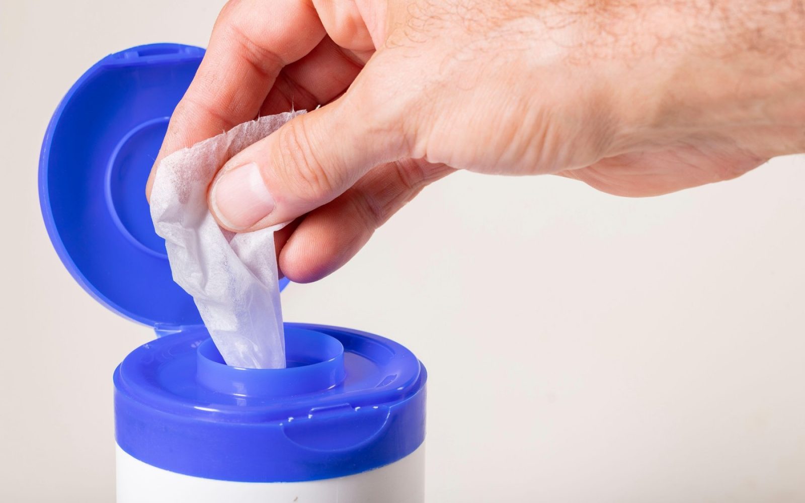 Bele krpice, namočene v razkužilo, ki jih je izvlekel moški. Pribor za dekontaminacijo površin v gospodinjstvu. Izolirano ozadje.