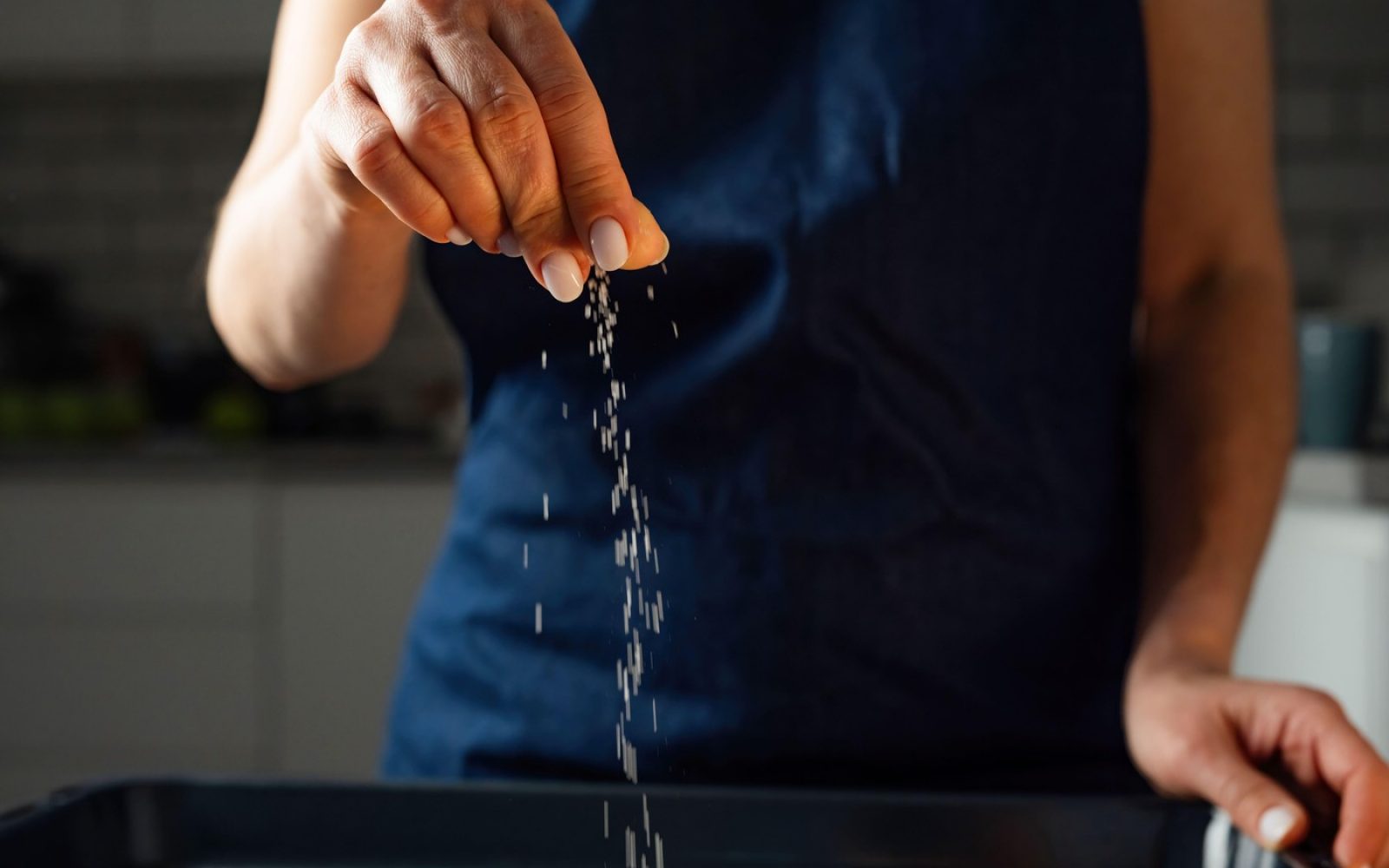 Ženska v kuhinji solijo hrano s ščepcem soli.