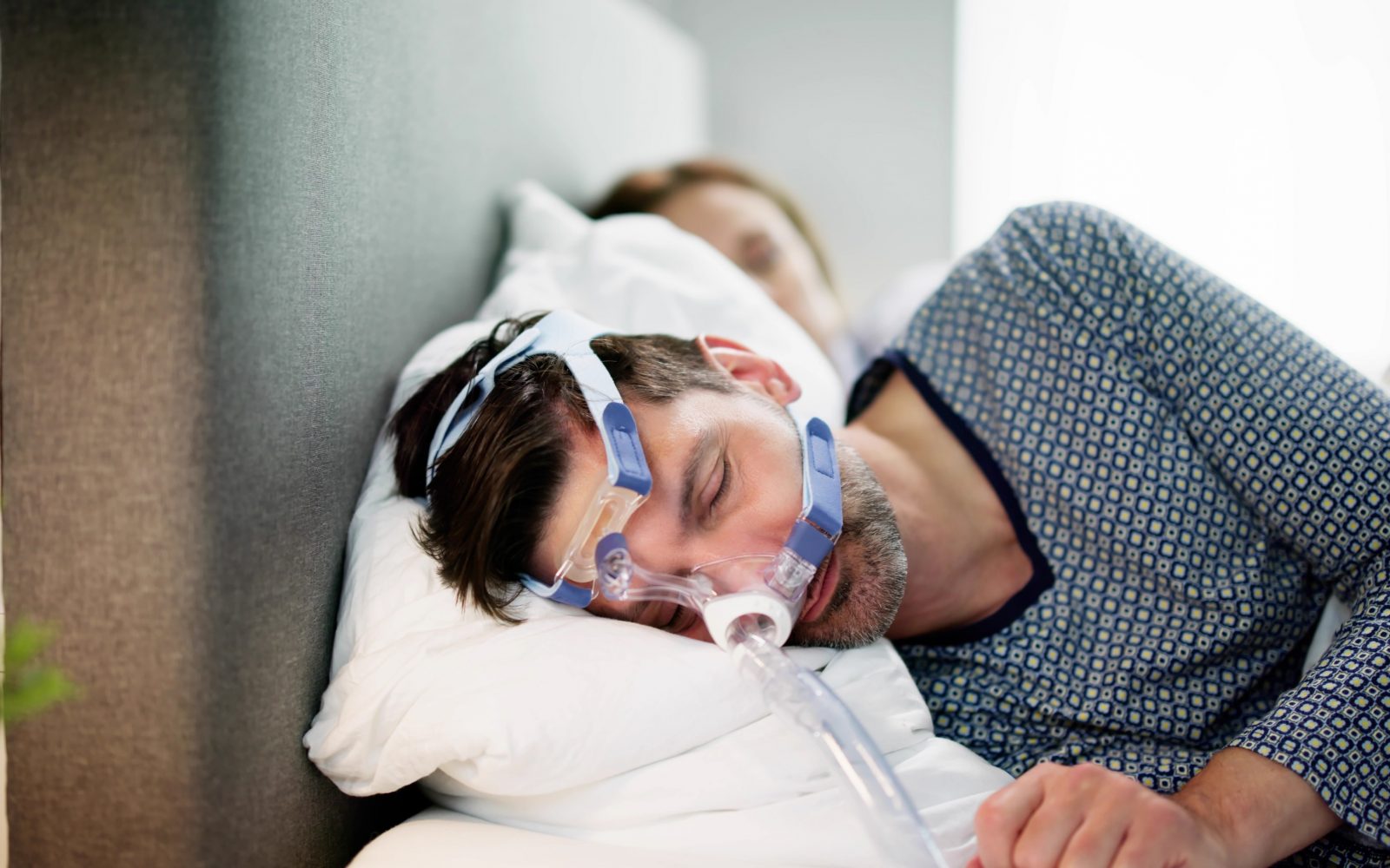 Moški spi z masko, ki mu olajša simptome spalne apneje.