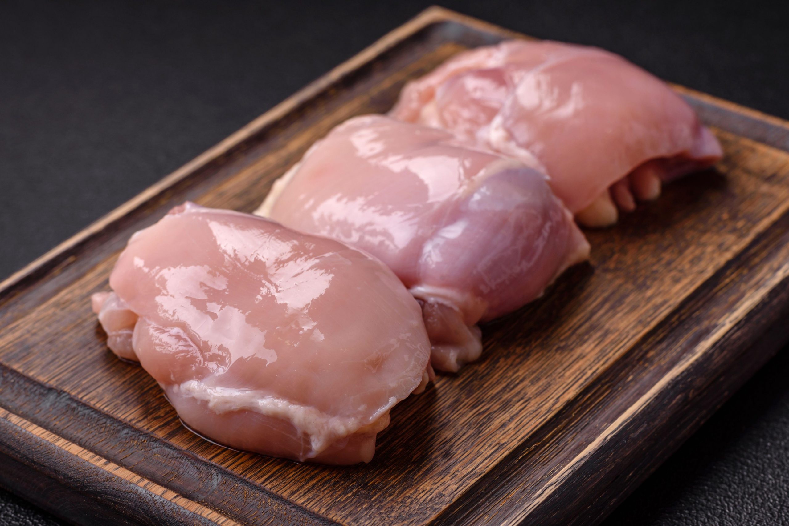 Kosi svežega surovega piščančjega mesa na rezalni deski.
