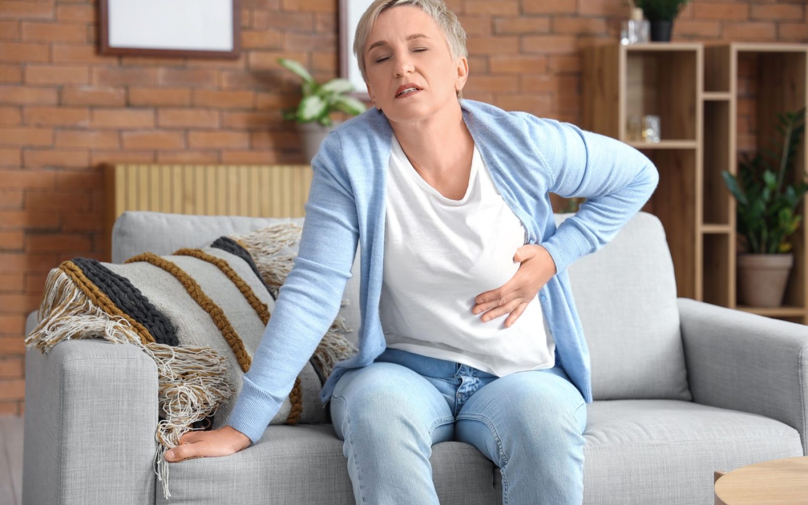 Ženska na kavču s simptomi srčnega infarkta – bolečina v prsih.