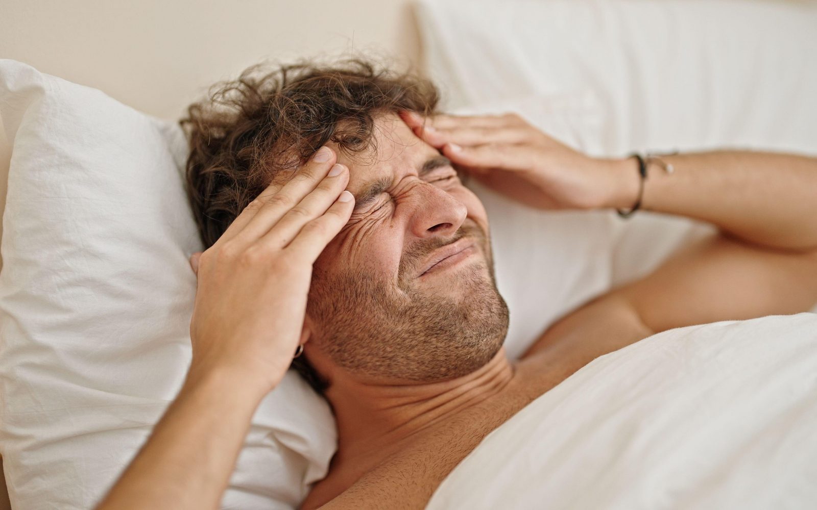 Mlad moški leži v postelji in se drži za glavo zaradi bolečine, ki je stranski učinek postenja z vodo.