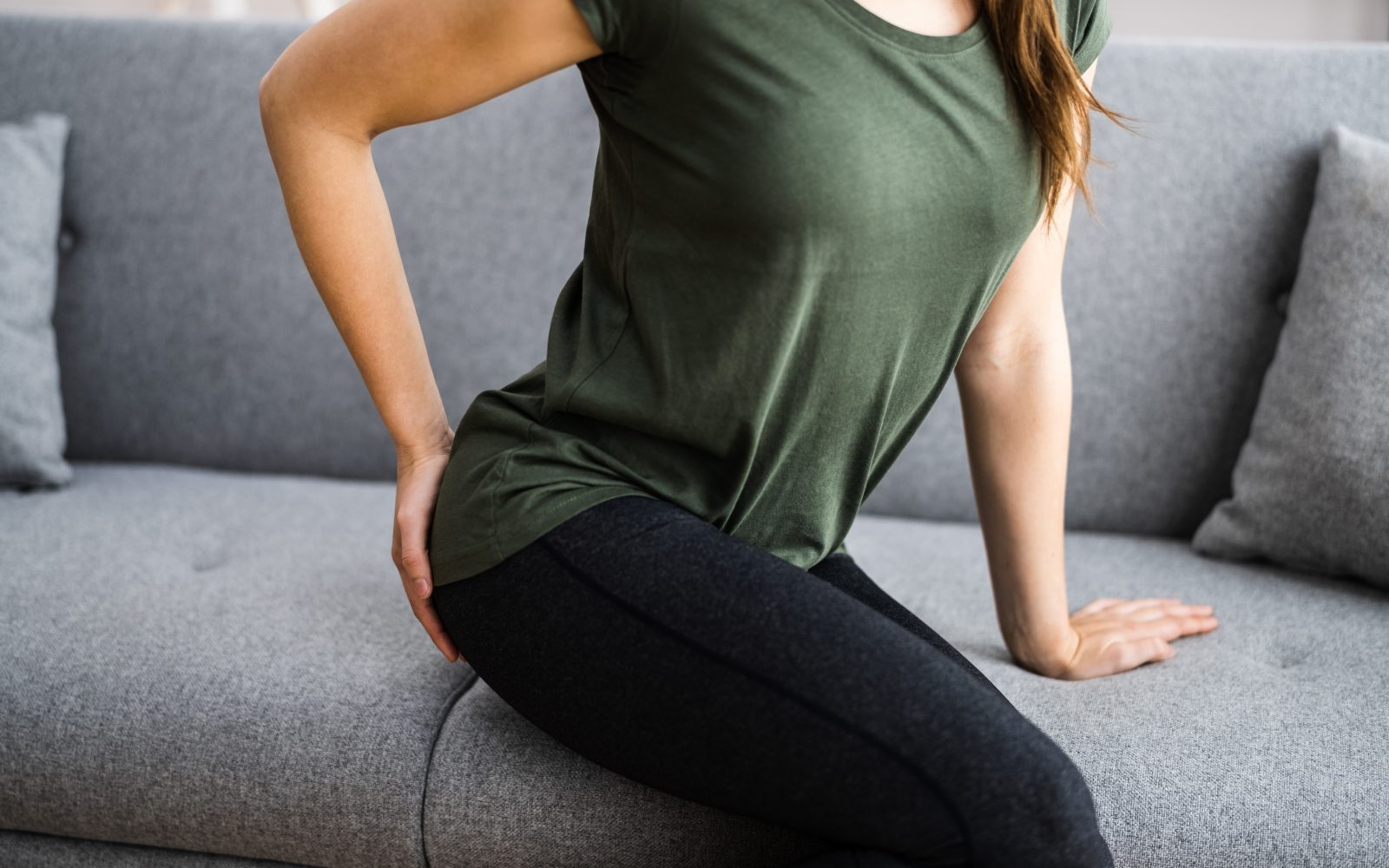 Ženska s težavo sedi na kavču zaradi hemoroidov