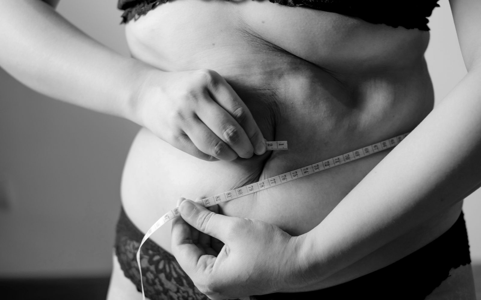 Ženska si meri obseg pasu, simbolika debelosti