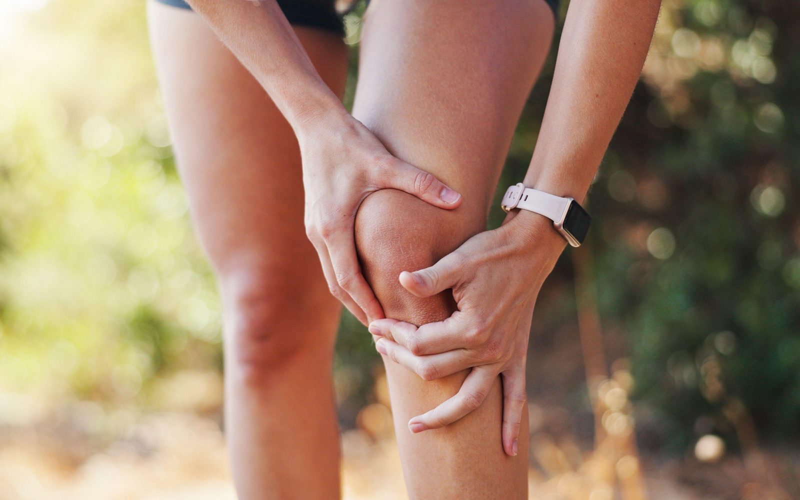 Mlada ženska se zunaj drži za koleno - je pokanje in praskanje v kolenih razlog za skrb?