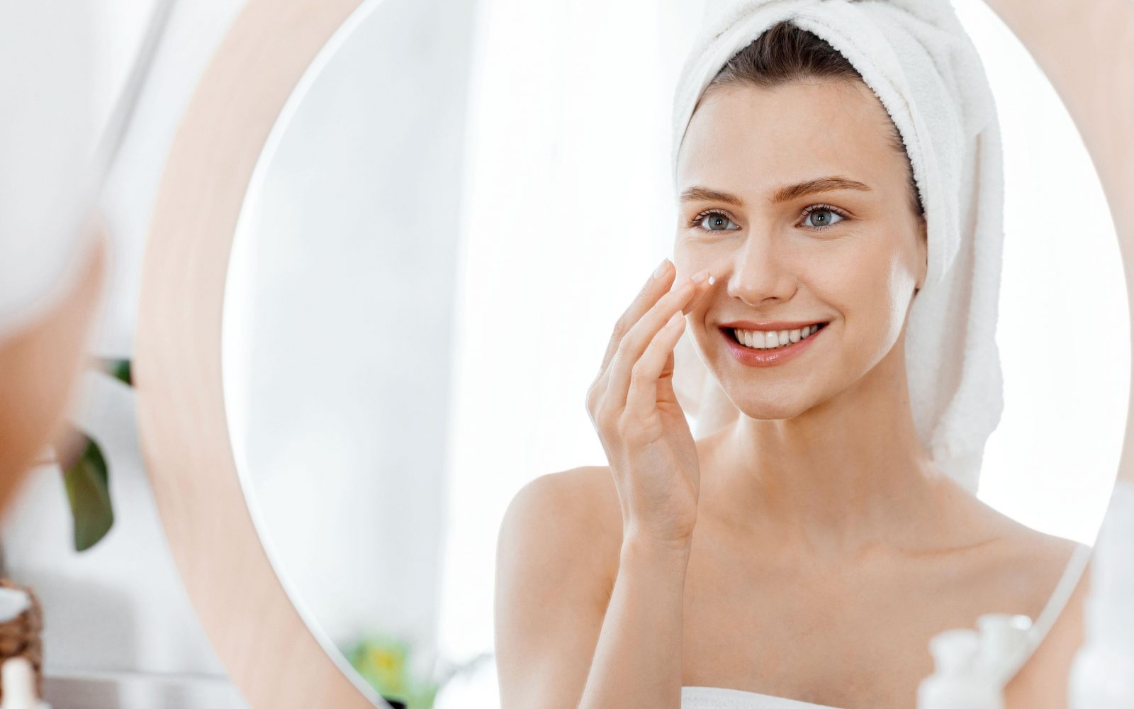 Mlada ženska si zvečer po tuširanju nanaša vlažilno kremo in vazelin na obraz - nega za prožno, sijočo in mehko kožo.