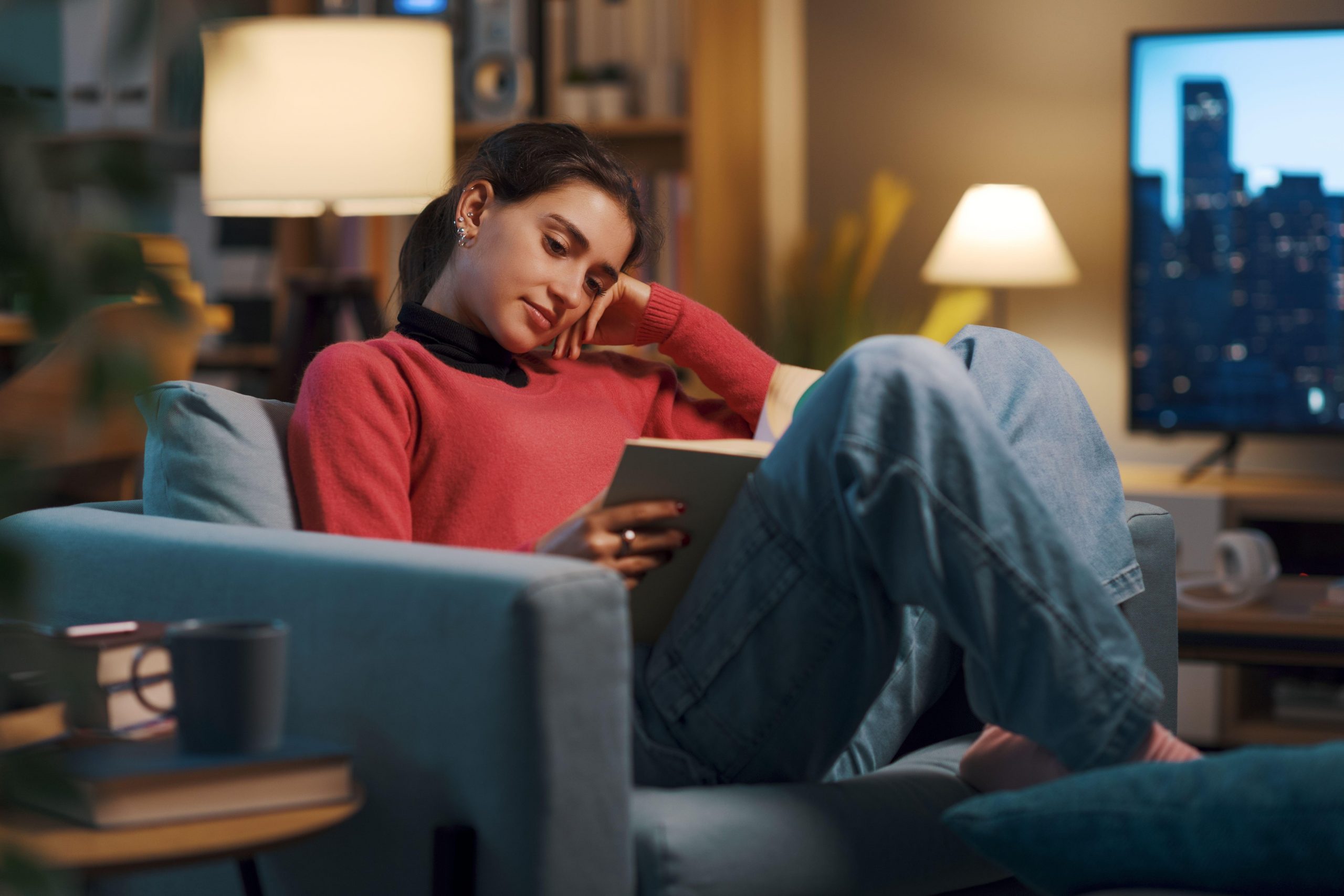 Mlada ženska se sprošča na kavču, bere knjigo in pije čaj - način za obvladovanje stresa, ki vpliva tako na duševno zdravje kot tudi na vzdrževanje zdrave telesne teže in izgubo kilogramov.